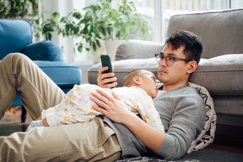 father laying with child looking at phone deciding whether to pay loans or buy house